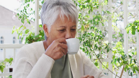 Happy-senior-mixed-race-woman-enjoying-a-coffee-in-garden
