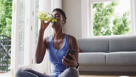 Mujer-Afroamericana-Bebiendo-Agua-Y-Usando-Un-Teléfono-Inteligente-En-Casa