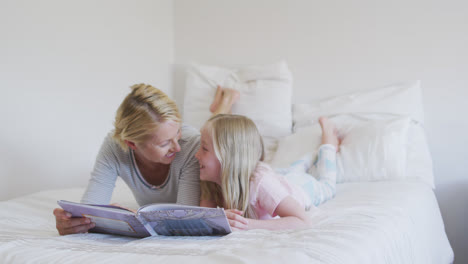 Side-view-of-a-Caucasian-woman-reading-a-story-to-her-daughter-on-bed