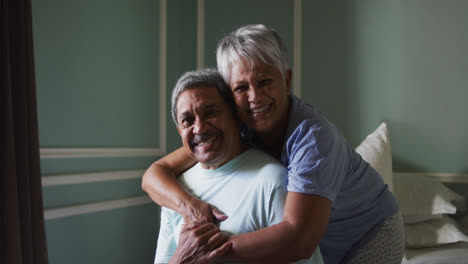 Senior-mixed-race-couple-embracing-and-laughing-in-bedroom