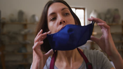 Female-potter-wearing-face-mask-and-apron-at-pottery-studio