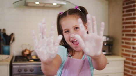 Porträt-Eines-Kaukasischen-Mädchens,-Das-In-Der-Küche-Zu-Hause-Eine-Schürze-Mit-Mehlpulver-An-Den-Händen-Trägt
