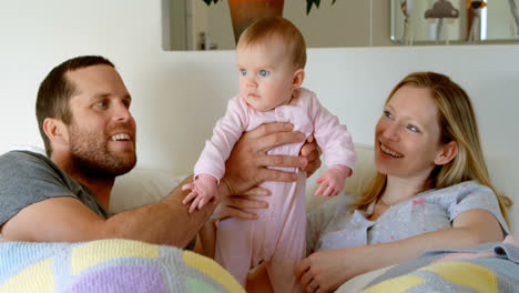 Front-view-of-mid-adult-caucasian-parents-playing-and-holding-baby-on-bed-in-a-comfortable-home-4k