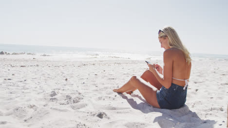Caucasian-woman-using-her-smartphone-on-the-beach