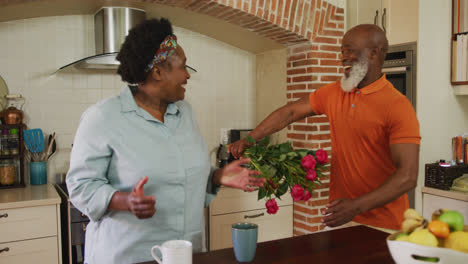 Afroamerikanischer-älterer-Mann-Schenkt-Einer-älteren-Frau-In-Der-Küche-Zu-Hause-Einen-Blumenstrauß