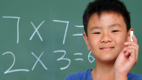 Front-view-of-Asian-schoolboy-standing-against-chalkboard-and-showing-chalk-in-classroom-4k