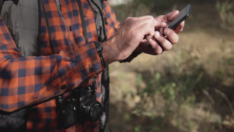 Close-up-view-of-senior-man-holding-smartphone-in-forest