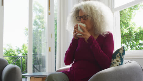 Ältere-Kaukasische-Frau-Trinkt-Kaffee,-Während-Sie-Zu-Hause-Auf-Der-Couch-Sitzt