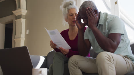 Stressed-mixed-race-senior-couple-discussing-finances-together-in-the-living-room-at-home