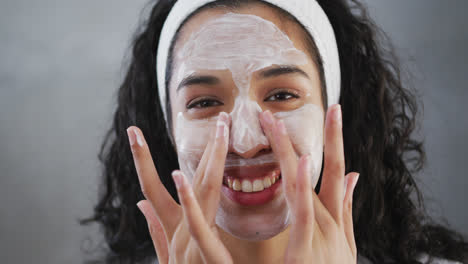 Portrait-of-smiling-mixed-race-woman-applying-face-cream-in-bathroom