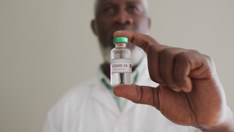 Close-up-of-male-african-american-doctor-holding-vaccine-bottle-at-hospital