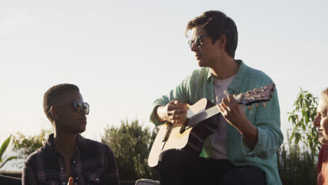 Young-man-playing-guitar-on-a-rooftop-with-his-friends