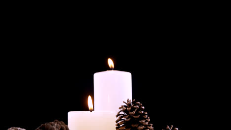 Burning-candles-and-pine-cones-against-black-background-4k