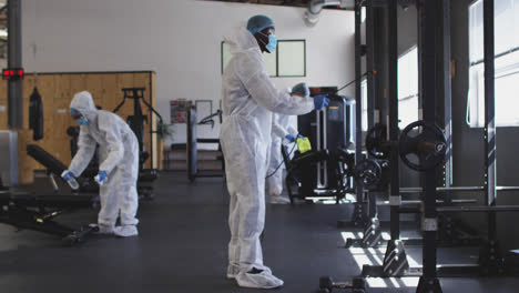 Team-of-health-workers-wearing-protective-clothes-cleaning-gym-by-using-disinfectant-sprayer