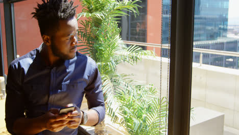 Front-view-of-young-black-businessman-using-mobile-phone-in-a-modern-office-4k