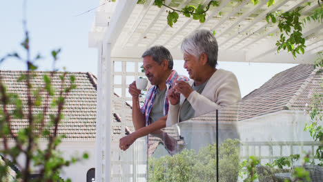 Senior-mixed-race-couple-drinking-coffee-on-balcony-in-garden