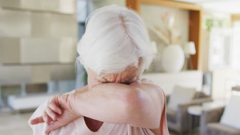 Senior-caucasian-woman-sneezing-on-her-elbow-at-home
