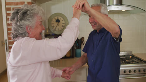 Senior-caucasian-couple-dancing-in-kitchen-in-slow-motion