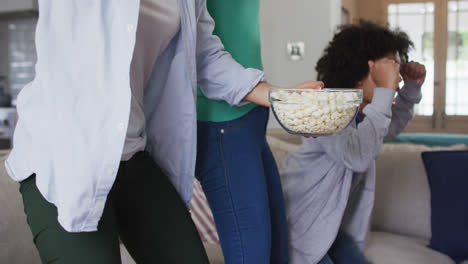 Mixed-race-lesbian-couple-and-daughter-watching-tv-eating-popcorn