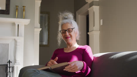 Senior-caucasian-woman-reading-a-book-while-sitting-on-the-couch-at-home