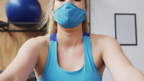 Caucasian-woman-wearing-face-mask-exercising-at-gym