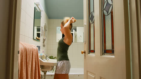 Woman-tying-her-hair-in-bathroom-at-home-4k