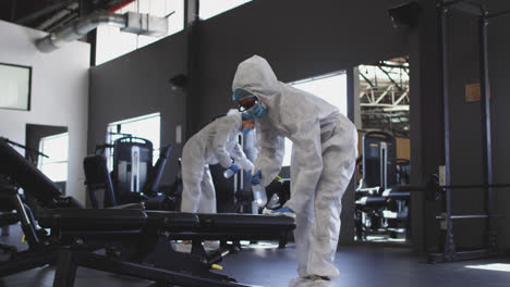 Team-of-health-workers-wearing-protective-clothes-cleaning-gym-by-using-disinfectant-sprayer