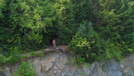 Female-hiker-standing-on-cliff-in-forest-4k