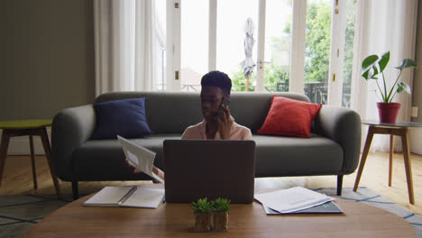 African-american-woman-holding-a-document-talking-on-smartphone-while-working-from-home