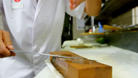 Chef-Masculino-Afilando-Un-Cuchillo-En-Una-Piedra-De-Afilar-En-La-Cocina-4k