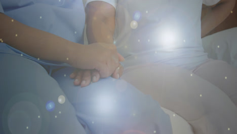 Spots-of-light-against-mid-section-of-health-worker-holding-patients-hand-