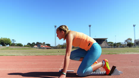 Side-view-of-Caucasian-female-athlete-taking-starting-position-on-a-running-track-at-sports-venue-4k