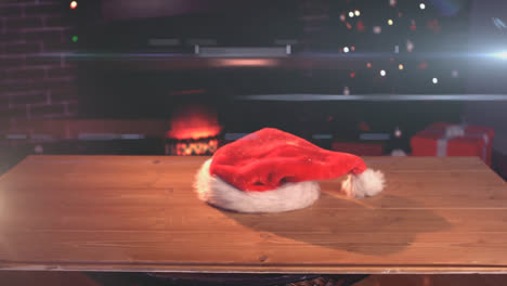 Digital-composition-of-glowing-spot-of-light-against-santa-hat-falling-on-wooden-surface