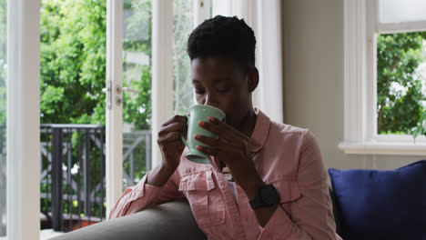Afroamerikanische-Frau-Trinkt-Kaffee,-Während-Sie-Zu-Hause-Auf-Der-Couch-Sitzt