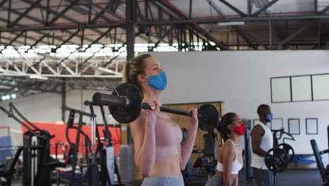 Fit-caucasian-woman-wearing-face-mask-exercising-using-barbell-in-the-gym