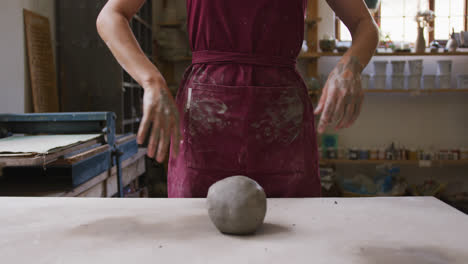 Mid-section-of-female-potter-wiping-her-hands-on-apron-at-pottery-studio