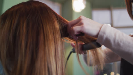 Female-hairdresser-straightening-hair-of-female-customer-at-hair-salon