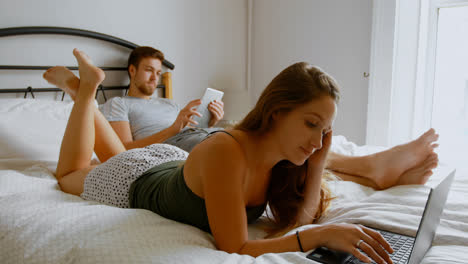 Couple-using-laptop-and-digital-tablet-on-bed-4k-