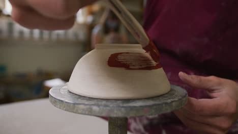 Close-up-view-of-female-potter-wearing-apron-painting-pot-on-potters-wheel-at-pottery-studio