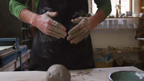Mid-section-of-male-potter-wiping-his-hands-on-apron-at-pottery-studio