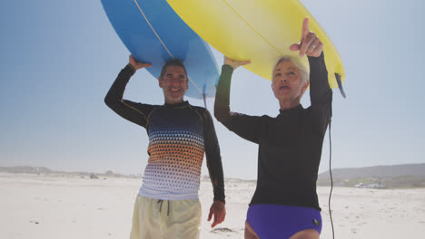 Senior-Caucasian-couple-holding-surfboards-above-their-heads-on-the-beach