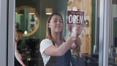 Female-hairdresser-changing-sign-board-from-Closed-to-Open-at-hair-salon