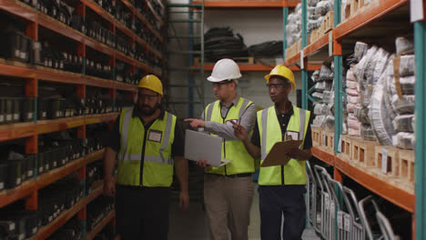 Two-Caucasian-and-an-African-American-male-factory-worker-at-a-factory-wearing-hard-hats-and-glasses