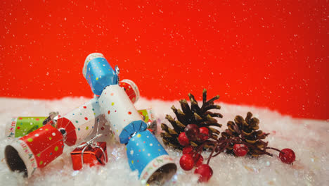 Animation-of-snow-falling-against-christmas-crackers-decorations-on-red