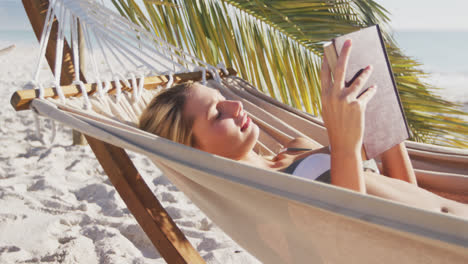 Caucasian-woman-lying-on-a-hammock-and-reading-a-book-on-the-beach
