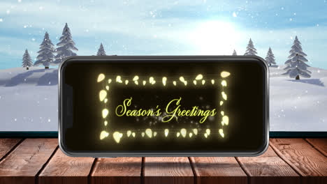 Digital-animation-of-seasons-greetings-text-and-fairy-lights-on-smartphone-screen-on-wooden-surface-