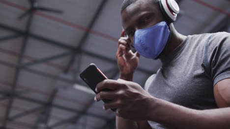 Afroamerikanischer-Mann-Mit-Gesichtsmaske-Benutzt-Smartphone-Im-Fitnessstudio