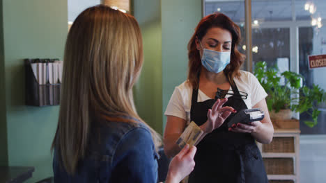Female-hairdresser-wearing-face-mask-receiving-payment-from-female-customer