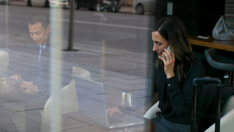 Side-view-of-beautiful-caucasian-businesswoman-talking-on-mobile-phone-and-working-on-using-laptop-i