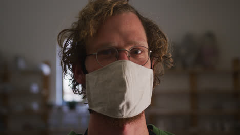 Portrait-of-male-potter-wearing-face-mask-and-apron-at-pottery-studio